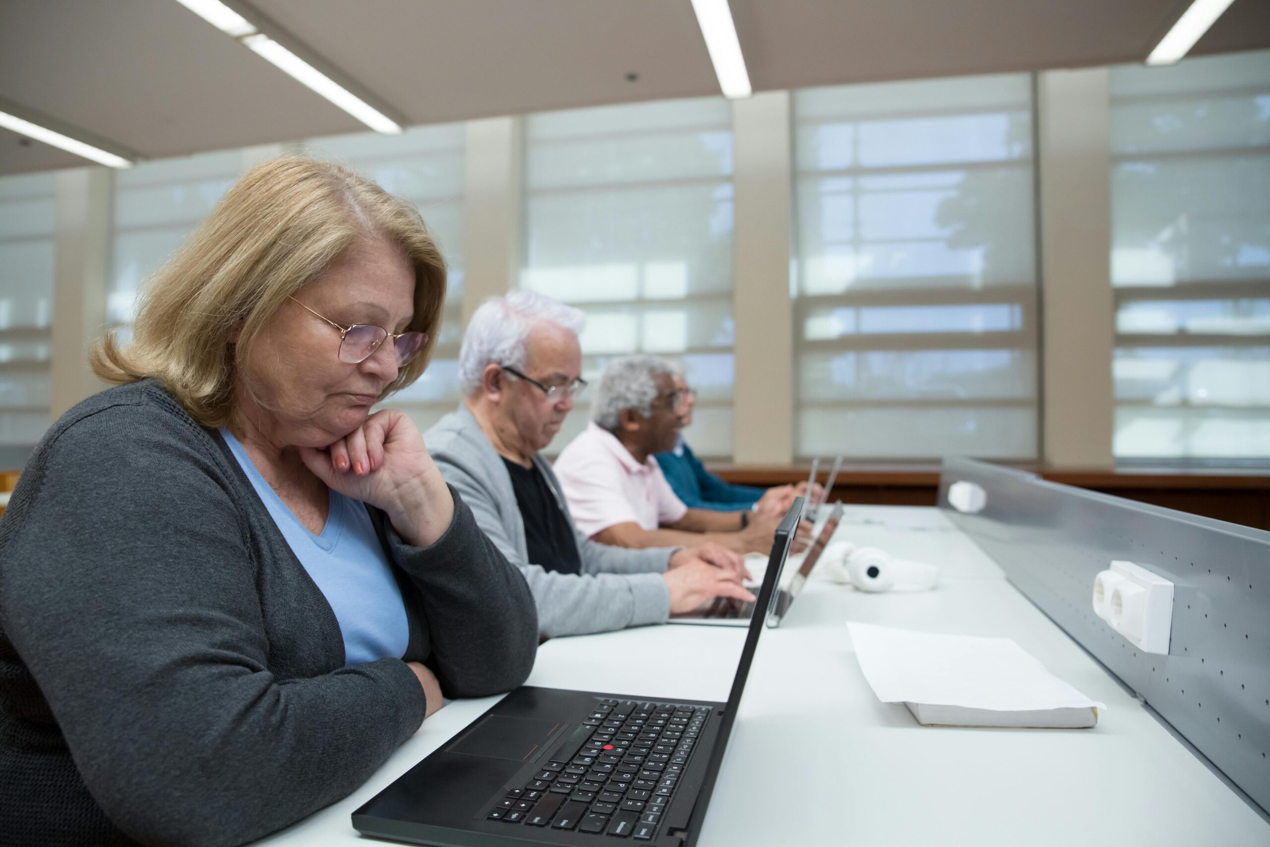 Seniors engaged in a computer class, learning digital skills with laptops indoors. structured learning vs personalised fluency coaching